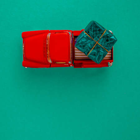 a miniature red car in the back carries a gift on a simple green-aquamarine background, top view. Save the space. Concept, festive Christmas mood, gift delivery. The trendの写真素材