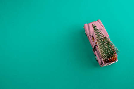 a miniature pink car in the back carries a Christmas tree on a simple blue-aquamarine background, top view. Save the space. Concept, festive Christmas mood, gift delivery. The trendの写真素材