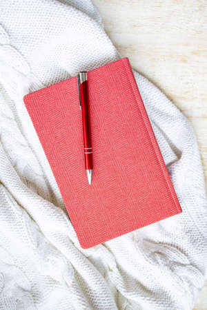 Paper red diary notebook and pen lies on a white knitted background, copy space.