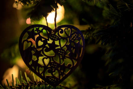toy in the shape of a heart hangs on a Christmas tree with glowing lights. Dark Silhouette.の写真素材