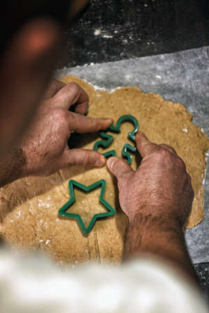 Young man in the process of baking Christmas dough, cutting gingerbread dough cookies. Festive mood. Family cooking concept, cooking process, new year traditions. The atmosphere of the holidayの写真素材