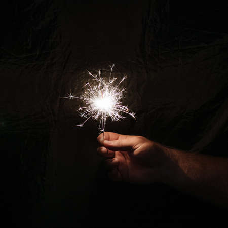 Hand with sparkler on dark background. Celebrating new year with sparkler. Hand holding sparkler on dark background. Christmas fun. New year concept.の写真素材