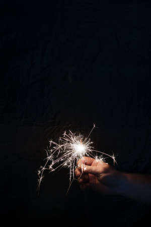 Hand with sparkler on dark background. Celebrating new year with sparkler. Hand holding sparkler on dark background. Christmas fun. New year concept.の写真素材