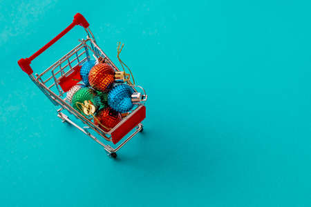 Grocery cart with Christmas balls toys on a blue-green simple background. Flat lay. Save the space. Postcard Template.の写真素材