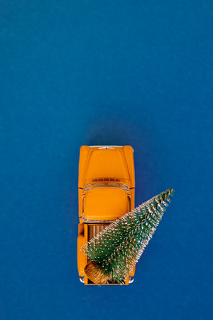 a miniature yellow car in the back carries a Christmas tree on a simple blue-aquamarine background, top view. Save the space. Concept, festive Christmas mood, gift delivery. The trendの写真素材