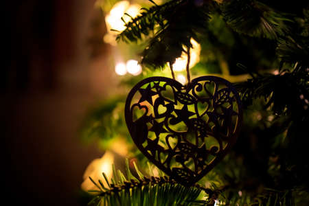 toy in the shape of a heart hangs on a Christmas tree with glowing lights. Dark Silhouette.の写真素材