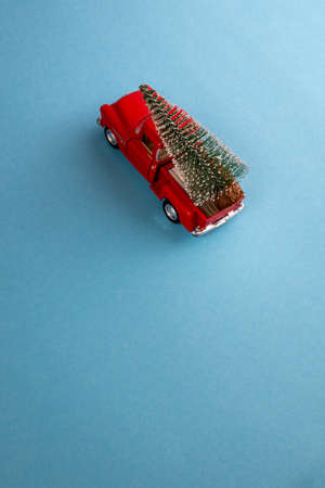 a miniature red car in the back carries a Christmas tree on a simple blue-aquamarine background, top view. Save the space. Concept, festive Christmas mood, gift delivery. The trendの写真素材
