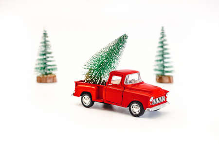 miniature red car in the back carries a Christmas tree on a white isolated background, top view. Save the space. Concept, festive Christmas mood, gift delivery. The trendの写真素材