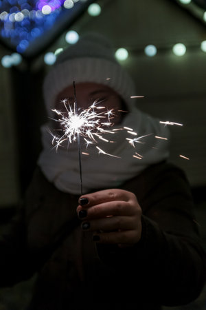 young happy woman in a winter hat holds a sparkler in front of her.の写真素材