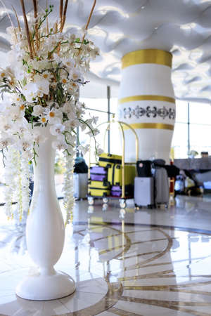 a lot of suitcases are on a trolley in a beautiful bright lobby of the hotel with flowers in a vase.の写真素材