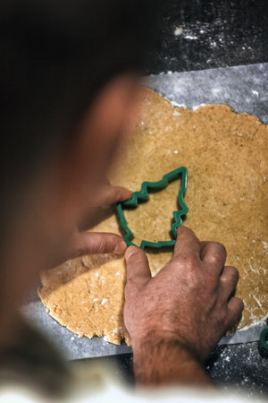 Young man in the process of baking Christmas dough, cutting gingerbread dough cookies. Festive mood. Family cooking concept, cooking process, new year traditions. The atmosphere of the holidayの写真素材