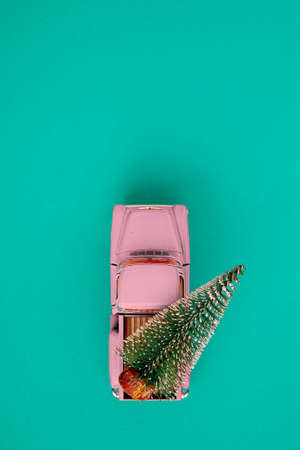a miniature pink car in the back carries a Christmas tree on a simple blue-aquamarine background, top view. Save the space. Concept, festive Christmas mood, gift delivery. The trendの写真素材