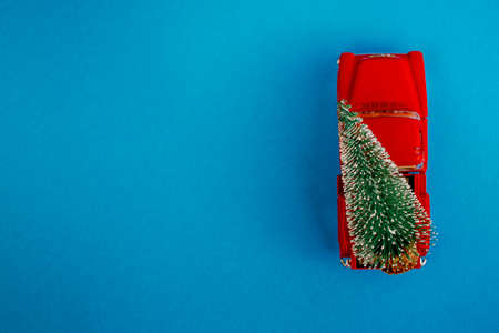 a miniature red car in the back carries a Christmas tree on a simple blue-aquamarine background, top view. Save the space. Concept, festive Christmas mood, gift delivery. The trendの写真素材