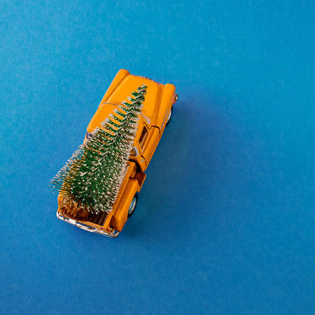 a miniature yellow car in the back carries a Christmas tree on a simple blue-aquamarine background, top view. Save the space. Concept, festive Christmas mood, gift delivery. The trendの写真素材