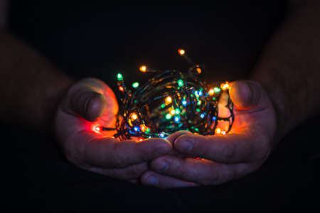 male hands holding a Christmas garland with lights on a dark background with copy space for text. Retro effect, close-up. Winter, postcard templateの写真素材