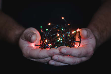 male hands holding a Christmas garland with lights on a dark background with copy space for text. Retro effect, close-up. Winter, postcard templateの写真素材
