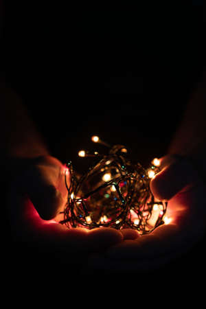male hands holding a Christmas garland with lights on a dark background with copy space for text. Retro effect, close-up. Winter, postcard templateの写真素材