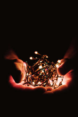 male hands holding a Christmas garland with lights on a dark background with copy space for text. Retro effect, close-up. Winter, postcard templateの写真素材