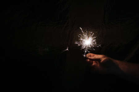 Hand with sparkler on dark background. Celebrating new year with sparkler. Hand holding sparkler on dark background. Christmas fun. New year conceptの写真素材