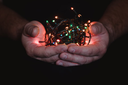 male hands holding a Christmas garland with lights on a dark background with copy space for text. Retro effect, close-up. Winter, postcard template.の写真素材