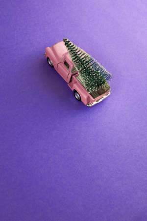 miniature pink car in the back carries a Christmas tree on a simple purple background, top view. Save the space. Concept, festive Christmas mood, gift delivery. The trend.の写真素材