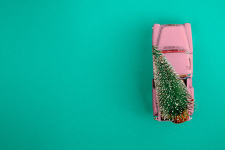 a miniature pink car in the back carries a Christmas tree on a simple blue-aquamarine background, top view. Save the space. Concept, festive Christmas mood, gift delivery. The trend.の写真素材