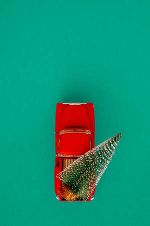 miniature red car in the back carries a Christmas tree on a simple green-aquamarine background, top view. Save the space. Concept, festive Christmas mood, gift delivery. The trend.の写真素材