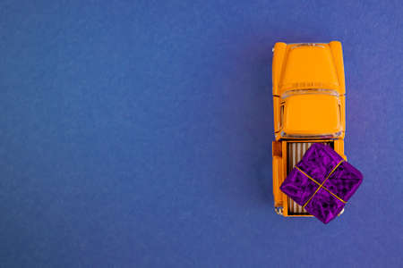 a miniature car in the back carries a gift on a simple blue-aquamarine background, top view. Save the space. Concept, festive Christmas mood, gift delivery. The trend.の写真素材