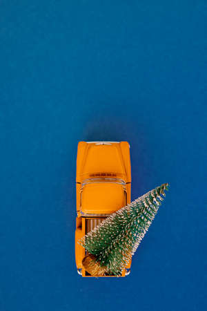 a miniature yellow car in the back carries a Christmas tree on a simple blue-aquamarine background, top view. Save the space. Concept, festive Christmas mood, gift delivery. The trend.の写真素材