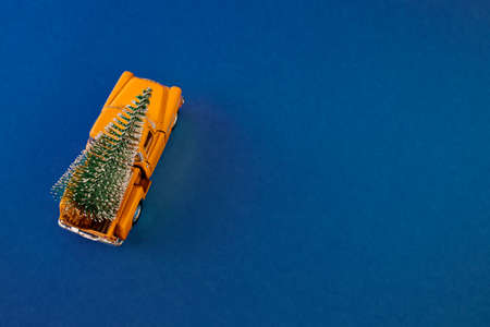 a miniature yellow car in the back carries a Christmas tree on a simple blue-aquamarine background, top view. Save the space. Concept, festive Christmas mood, gift delivery. The trend.の写真素材