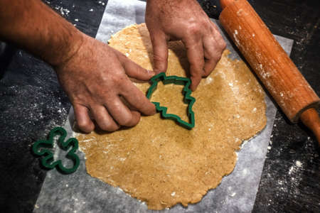 Young man in the process of baking Christmas dough, cutting gingerbread dough cookies. Festive mood. Family cooking concept, cooking process, new year traditions. The atmosphere of the holiday.の写真素材
