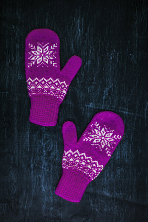 a pair of red-pink-lilac-magenta purple knitted mittens on a dark blue-green-brown woodenの写真素材
