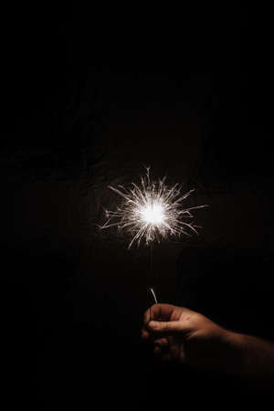 Hand with sparkler on dark background. Celebrating new year with sparkler. Hand holding sparkler on dark background. Christmas fun. New year conceptの写真素材