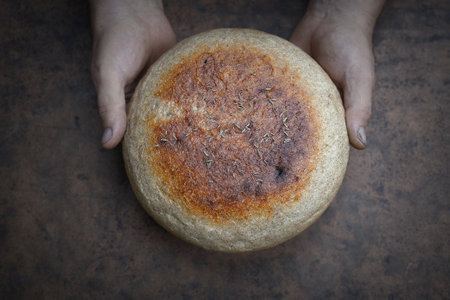 Homemade crusty loave of bread on wooden background. Baker holding fresh bread in the hands. view from above. Dark moodの写真素材