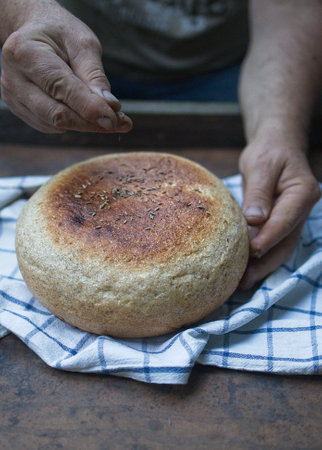The bakers hand sprinkles cumin on a fresh bun close-up. A man finishes baking, decorates warm...