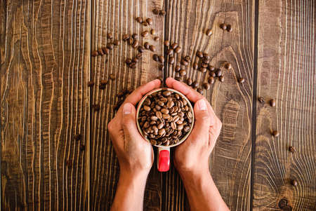 Hand held coffee cup full of roasted coffee beans.の写真素材