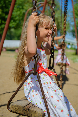 Happy little girl five years old wearing summer dress having fun on a swing in the park on a hot sunny summer dayの写真素材