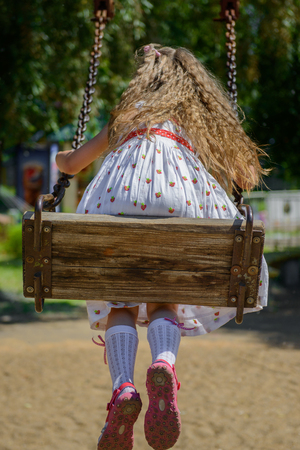 Happy little girl five years old wearing summer dress having fun on a swing in the park on a hot sunny summer dayの写真素材