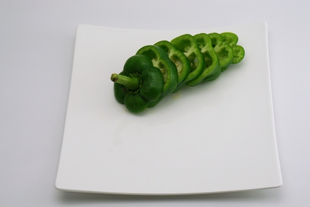 isolated green slightly cut sweet pepper on dishの写真素材