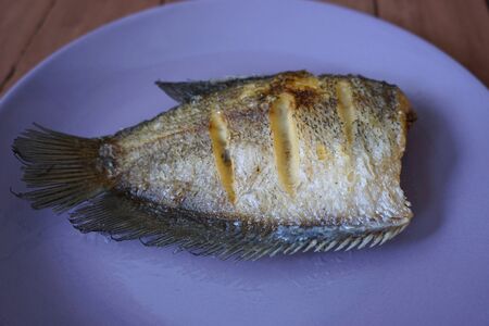 crispy fried Sepat siam fish on plate with the wood board background