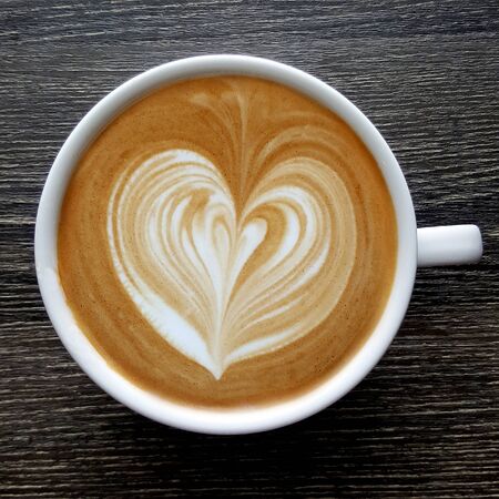 Top view of a mug of latte art coffee on timber background.