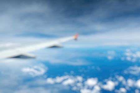 Out of Focus of Wing of an airplane flying above the clouds see through the window. Business...
