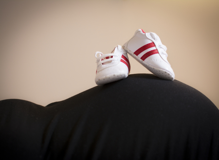 Pregnant woman with a pair of baby sneakers on the bellyの写真素材