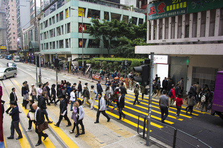 HONG KONG - DECEMBER 12, 2013: Pedestrians crossing the street in front of a tram station.のeditorial素材