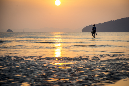 Young woman walking on seashore at sunset and looking at the sun over the Andaman sea in Ao Nang, Thailandの写真素材