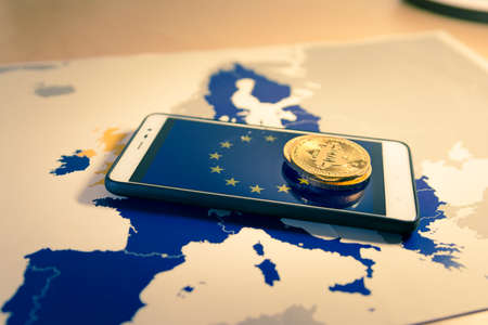 Financial concept with golden Bitcoin over smartphone, UE flag and map. Situation of Bitcoin and other cryptocurrencies in European Union concept. Warm moodの写真素材