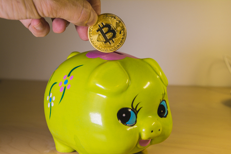 A green piggy bank with a golden bitcoin. Economical and financial concept involving cryptocoins, investment and savingsの写真素材
