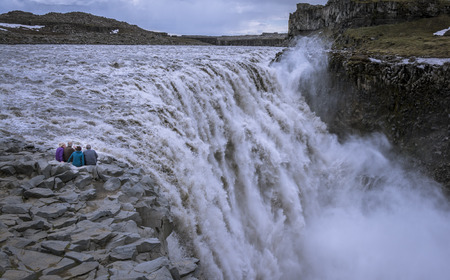 Senior travelers sitting on the edge, contemplating Detifoss waterfall. Retirees traveling arround...