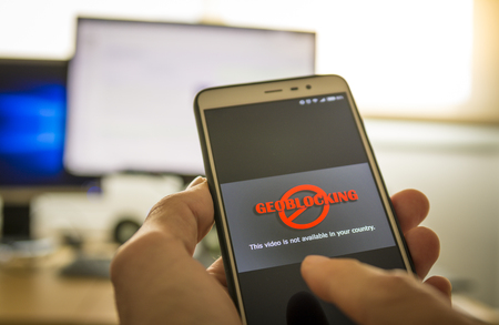 Hands using a smartphone with Geo-blocking on screen.の写真素材