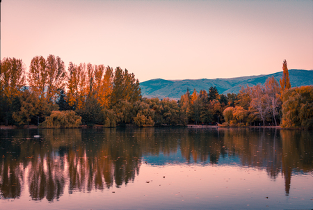 Teal and orange mood of autumn colors and reflection on the Puigcerdas pond waterの写真素材